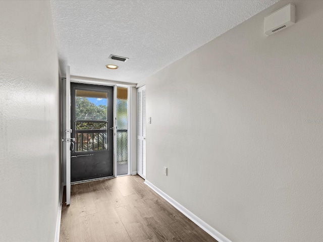 doorway to outside featuring a textured ceiling, wood finished floors, visible vents, and baseboards