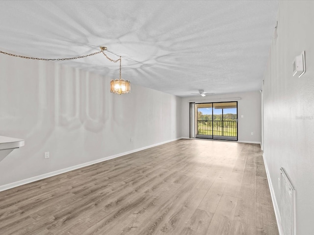 unfurnished room with visible vents, a textured ceiling, wood finished floors, baseboards, and ceiling fan with notable chandelier