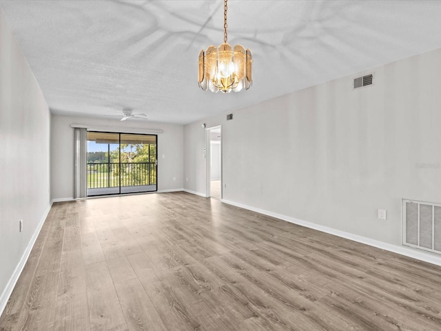 unfurnished room with a textured ceiling, wood finished floors, visible vents, and baseboards