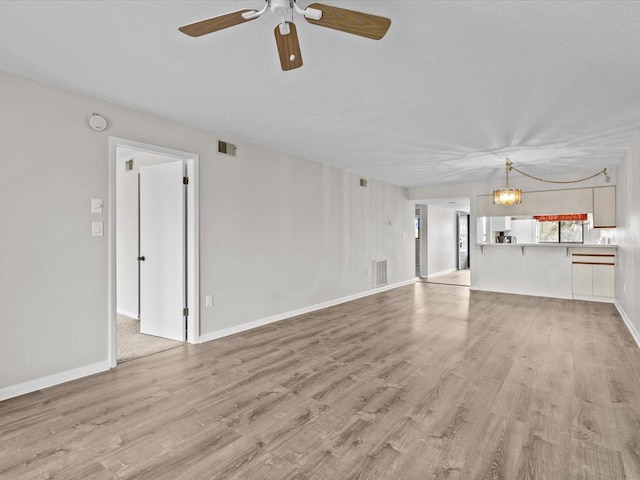 unfurnished living room with light wood-type flooring, visible vents, and ceiling fan with notable chandelier