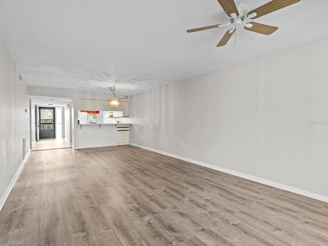 unfurnished living room with ceiling fan with notable chandelier, baseboards, and wood finished floors