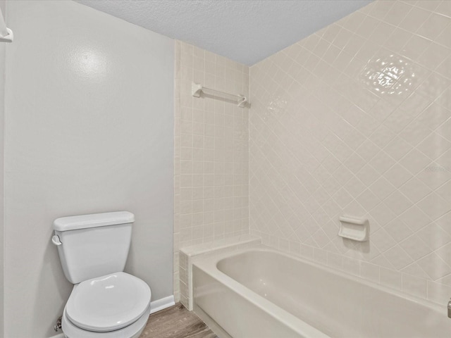 bathroom featuring baseboards, toilet, wood finished floors, a textured ceiling, and shower / bathing tub combination