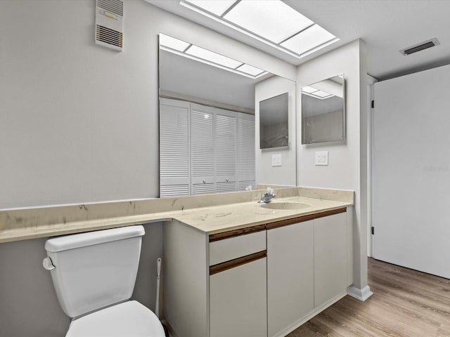 bathroom with toilet, visible vents, wood finished floors, and vanity