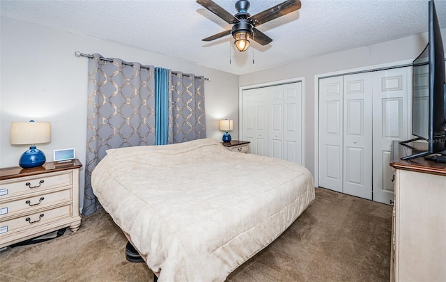 bedroom featuring dark carpet, ceiling fan, multiple closets, and a textured ceiling