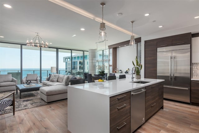 kitchen with light wood-type flooring, stainless steel appliances, a kitchen island with sink, sink, and dark brown cabinetry