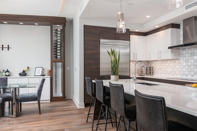 kitchen featuring light hardwood / wood-style floors, tasteful backsplash, hanging light fixtures, built in refrigerator, and wall chimney range hood