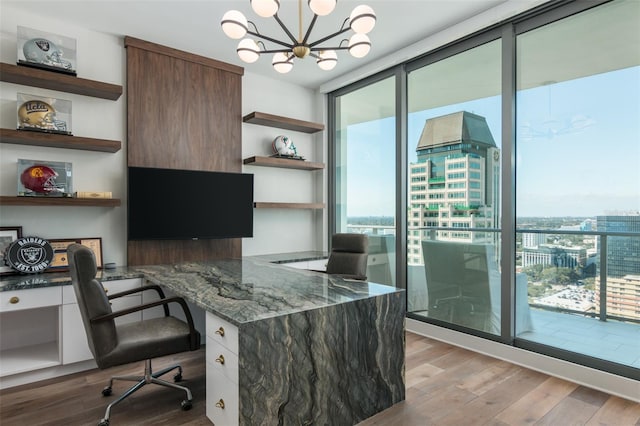 office with light wood-type flooring, built in desk, floor to ceiling windows, and a notable chandelier