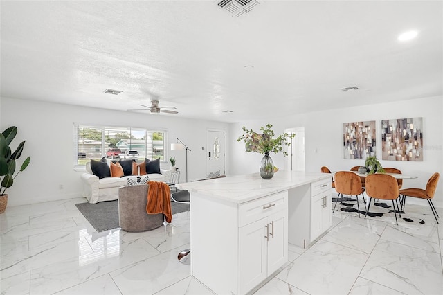 kitchen featuring white cabinetry, a center island, ceiling fan, light stone counters, and a textured ceiling