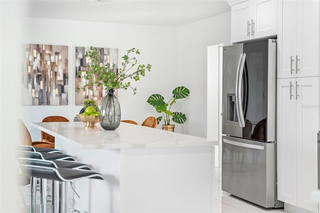 kitchen with stainless steel fridge, white cabinetry, a breakfast bar area, and light stone counters