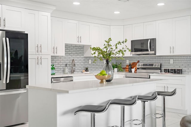 kitchen with a breakfast bar, backsplash, white cabinets, light stone countertops, and appliances with stainless steel finishes