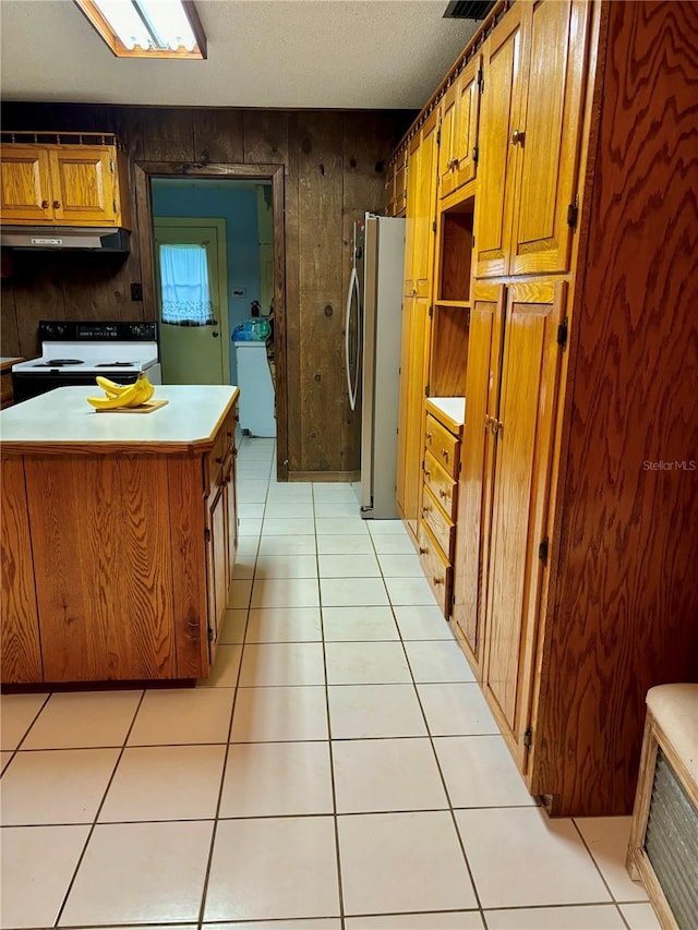 kitchen with a textured ceiling, wood walls, stainless steel fridge, white electric range oven, and light tile patterned flooring