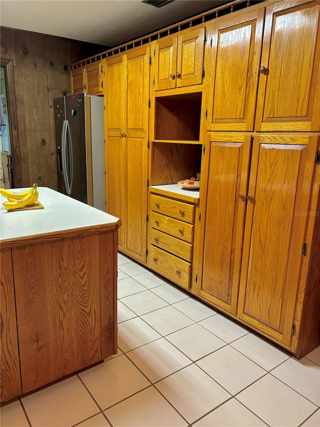 kitchen featuring light tile patterned floors, wooden walls, and stainless steel refrigerator with ice dispenser