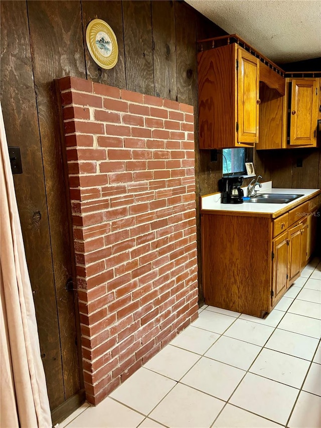 kitchen featuring brick wall, light tile patterned floors, sink, and a textured ceiling