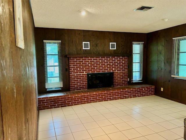 unfurnished living room featuring wood walls, a textured ceiling, and a brick fireplace