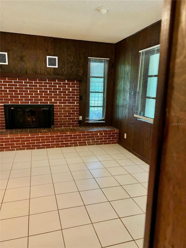 unfurnished living room with a textured ceiling, light tile patterned flooring, wood walls, and a fireplace