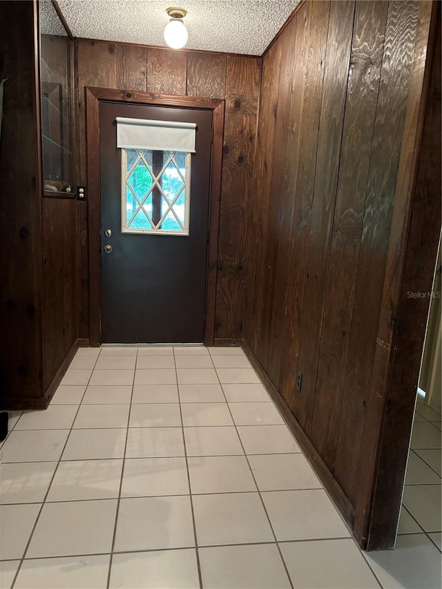 entryway featuring a textured ceiling, light tile patterned flooring, and wooden walls