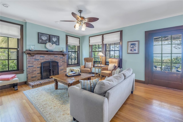 living room with light wood-type flooring, crown molding, a brick fireplace, and ceiling fan