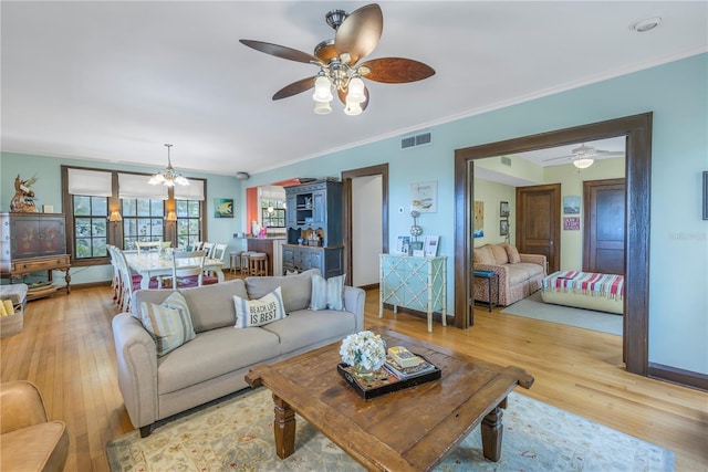 living room featuring ceiling fan with notable chandelier, ornamental molding, and light hardwood / wood-style floors