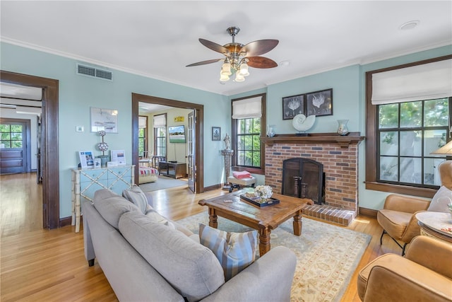 living room featuring ceiling fan, light hardwood / wood-style floors, crown molding, and a brick fireplace