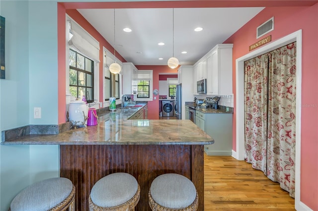 kitchen with washer and clothes dryer, hanging light fixtures, kitchen peninsula, sink, and light wood-type flooring