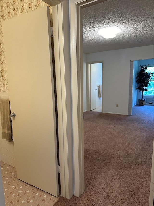 hall with light colored carpet and a textured ceiling