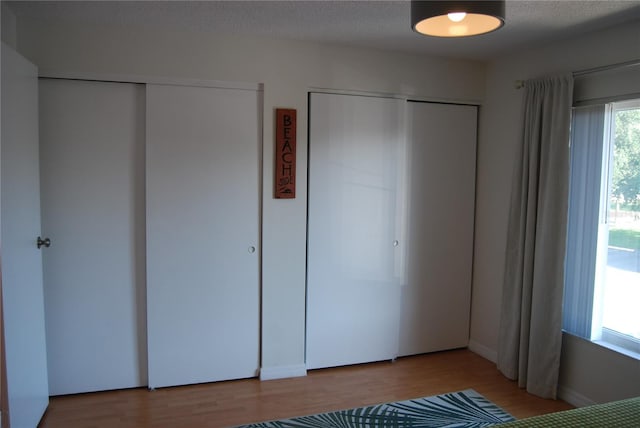 unfurnished bedroom with two closets, light wood-type flooring, multiple windows, and a textured ceiling