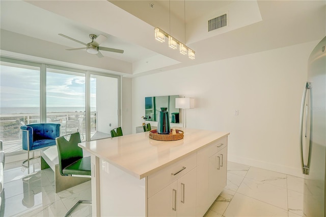 kitchen with a center island, white cabinetry, stainless steel fridge, a raised ceiling, and ceiling fan