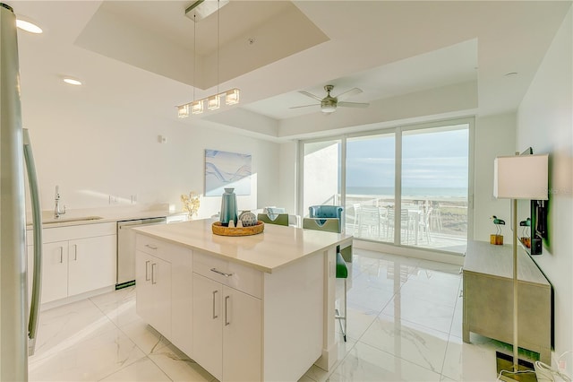 kitchen with a raised ceiling, dishwasher, a center island, white cabinetry, and ceiling fan