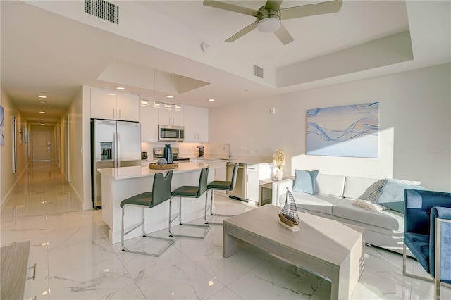 tiled living room with a raised ceiling, ceiling fan, and sink