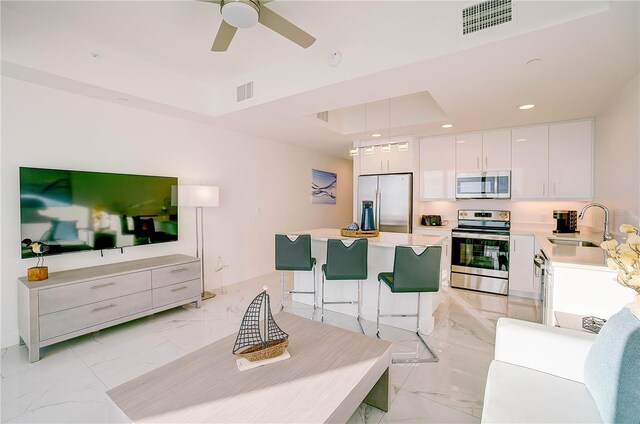 living room featuring a raised ceiling, ceiling fan, sink, and light tile patterned floors