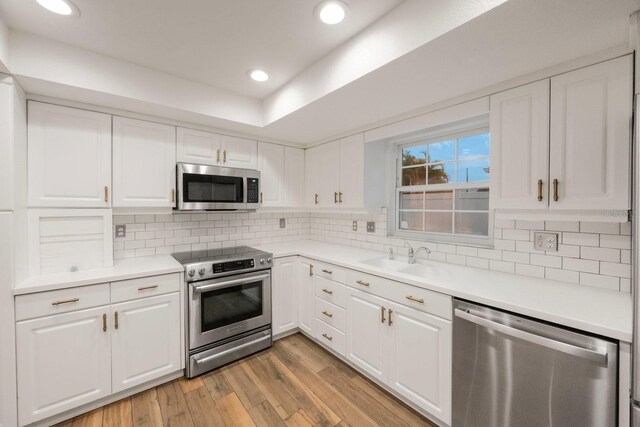 kitchen with backsplash, light wood-type flooring, appliances with stainless steel finishes, and white cabinets