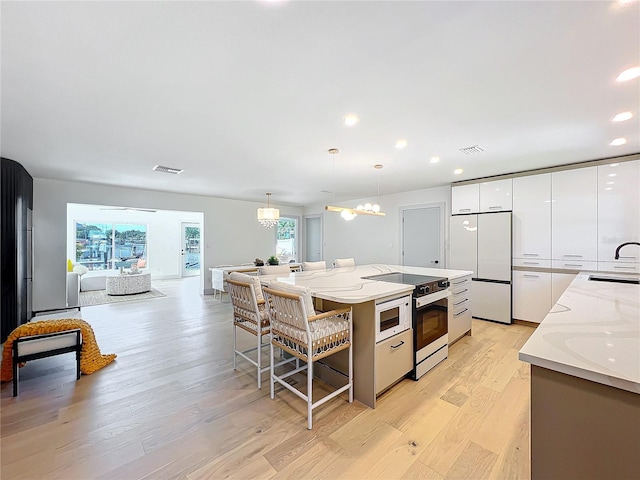 kitchen with built in appliances, a spacious island, decorative light fixtures, light stone countertops, and white cabinets