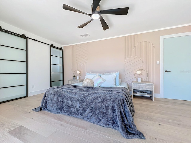 bedroom with crown molding, light hardwood / wood-style flooring, ceiling fan, and a barn door