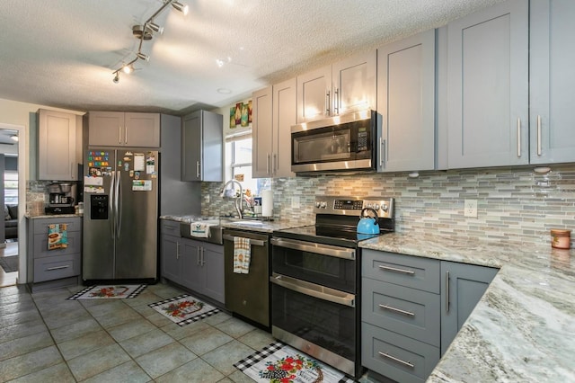 kitchen featuring gray cabinetry, decorative backsplash, light tile patterned flooring, light stone counters, and stainless steel appliances