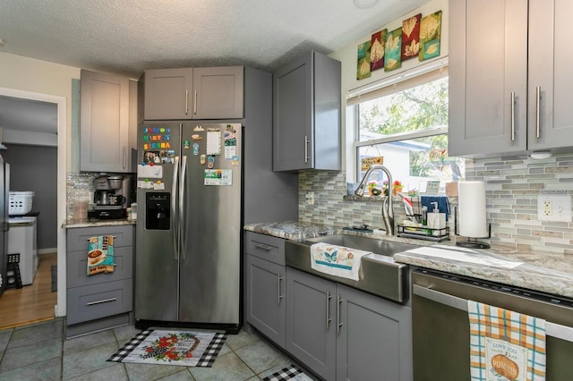 kitchen featuring gray cabinets, appliances with stainless steel finishes, light stone countertops, and tasteful backsplash