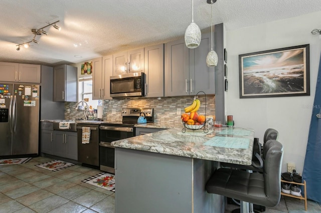 kitchen with kitchen peninsula, gray cabinetry, decorative light fixtures, backsplash, and appliances with stainless steel finishes