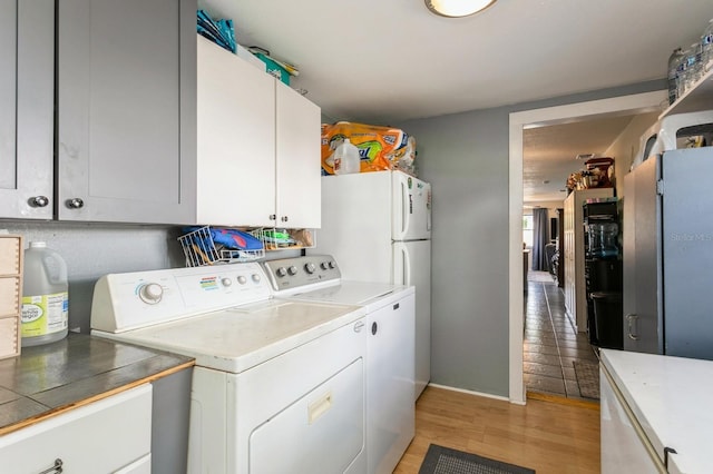 clothes washing area with cabinets, light wood-type flooring, and washing machine and dryer