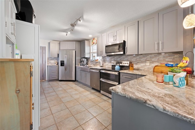 kitchen featuring appliances with stainless steel finishes, gray cabinetry, backsplash, light stone counters, and a textured ceiling