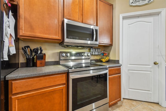 kitchen featuring light tile patterned floors, stainless steel appliances, dark countertops, and brown cabinets