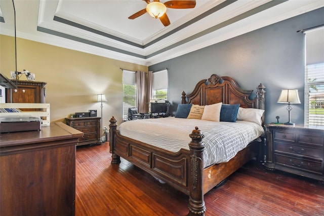 bedroom with ornamental molding, a raised ceiling, dark wood finished floors, and a ceiling fan