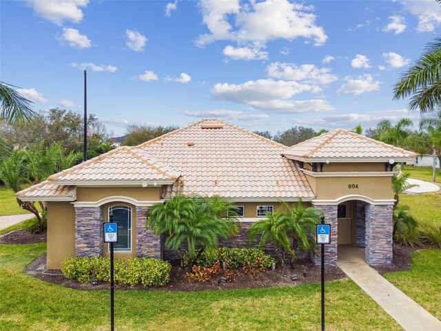 mediterranean / spanish home featuring stone siding, a front yard, a tiled roof, and stucco siding