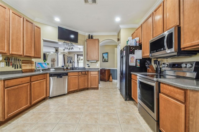 kitchen with arched walkways, crown molding, dark countertops, appliances with stainless steel finishes, and light tile patterned flooring