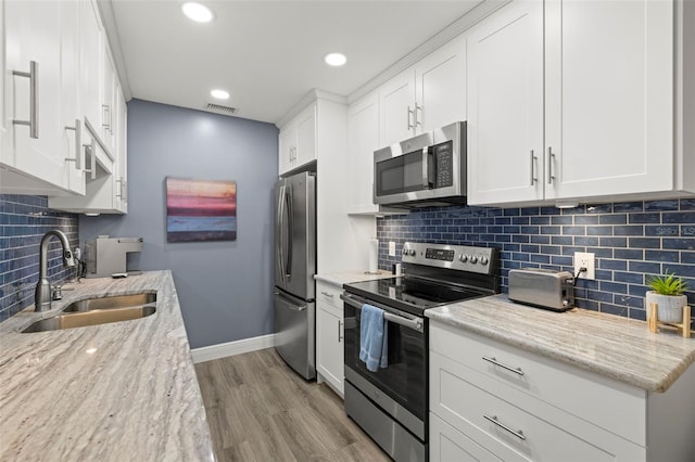 kitchen with baseboards, white cabinets, appliances with stainless steel finishes, light wood-style floors, and a sink