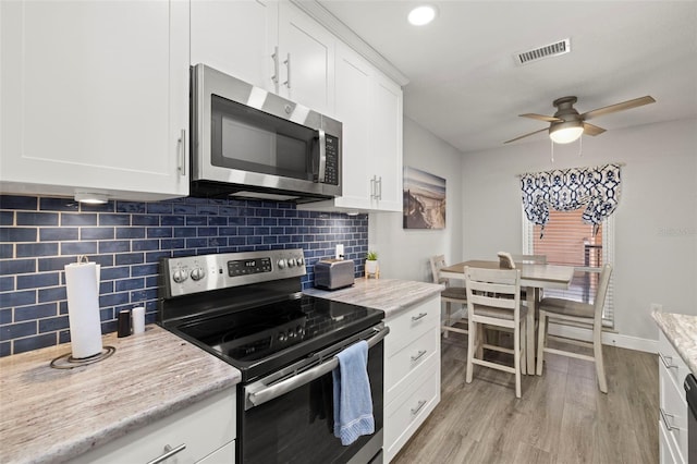 kitchen with white cabinets, light wood-type flooring, appliances with stainless steel finishes, ceiling fan, and decorative backsplash