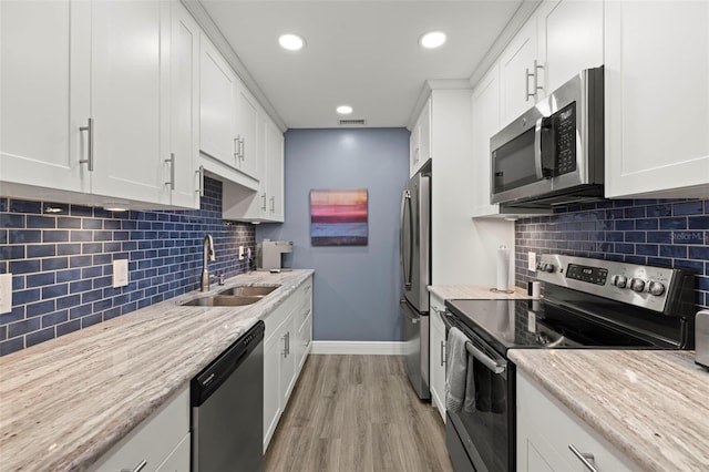 kitchen with light wood-type flooring, white cabinetry, stainless steel appliances, sink, and decorative backsplash