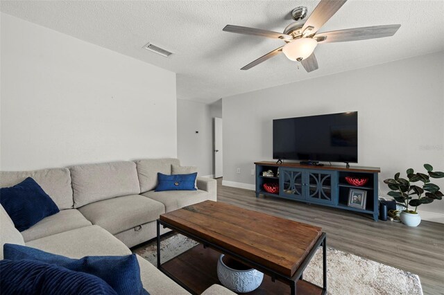 living room with ceiling fan, hardwood / wood-style flooring, and a textured ceiling