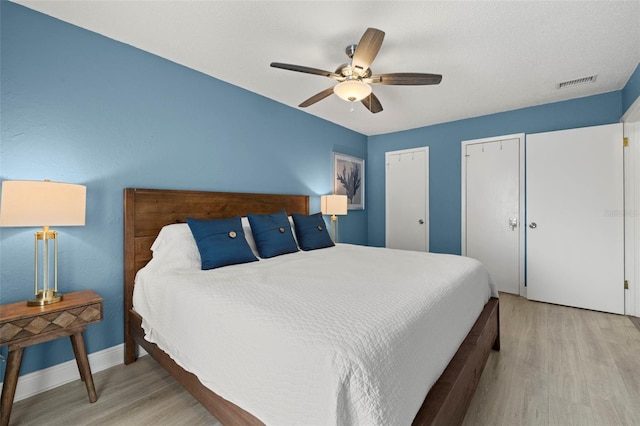 bedroom with light wood-type flooring, ceiling fan, and multiple closets