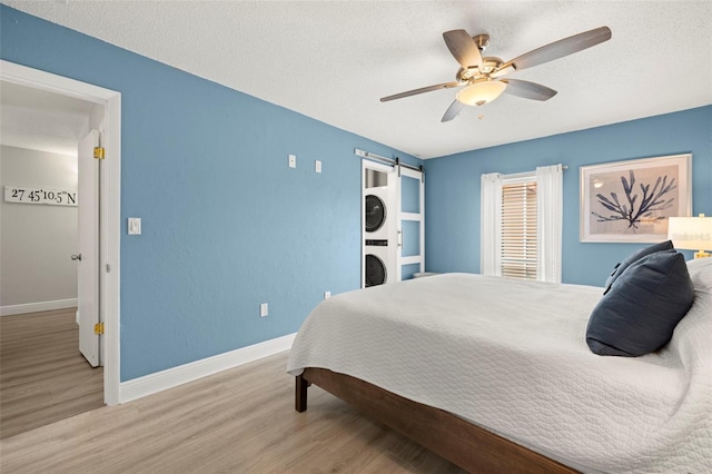 bedroom with a textured ceiling, wood-type flooring, ceiling fan, and a barn door