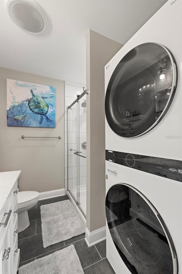 laundry area with dark tile patterned floors and stacked washer / drying machine