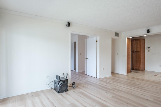 empty room with light wood-type flooring, crown molding, and a textured ceiling